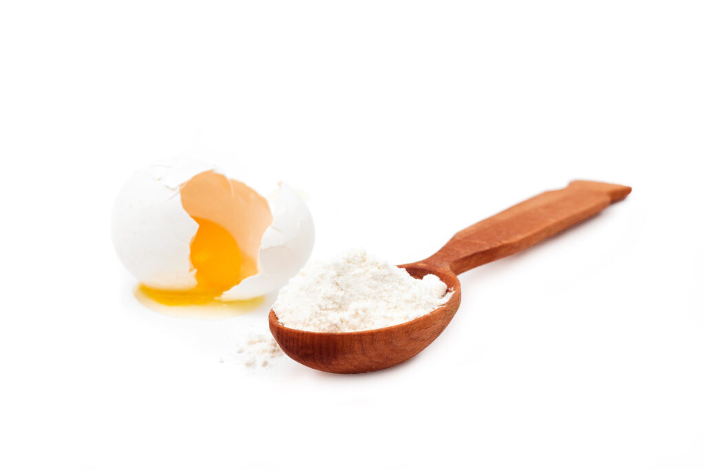 Cracked egg next to a wooden spoon of egg powder